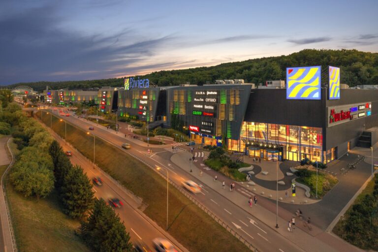 Centrum handlowe Riviera o zmierzchu z widokiem na wejście i parking.