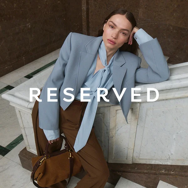 Kobieta w eleganckim niebieskim żakiecie i brązowych spodniach.