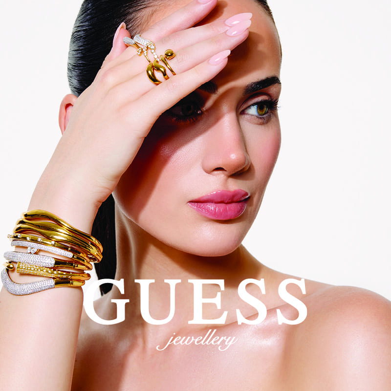 Modelka prezentuje biżuterię Guess z bransoletkami i pierścionkami.