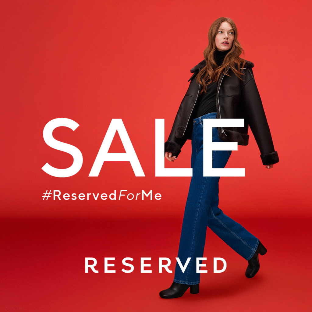 Modelka w kurtce i dżinsach na czerwonym tle z napisem SALE.