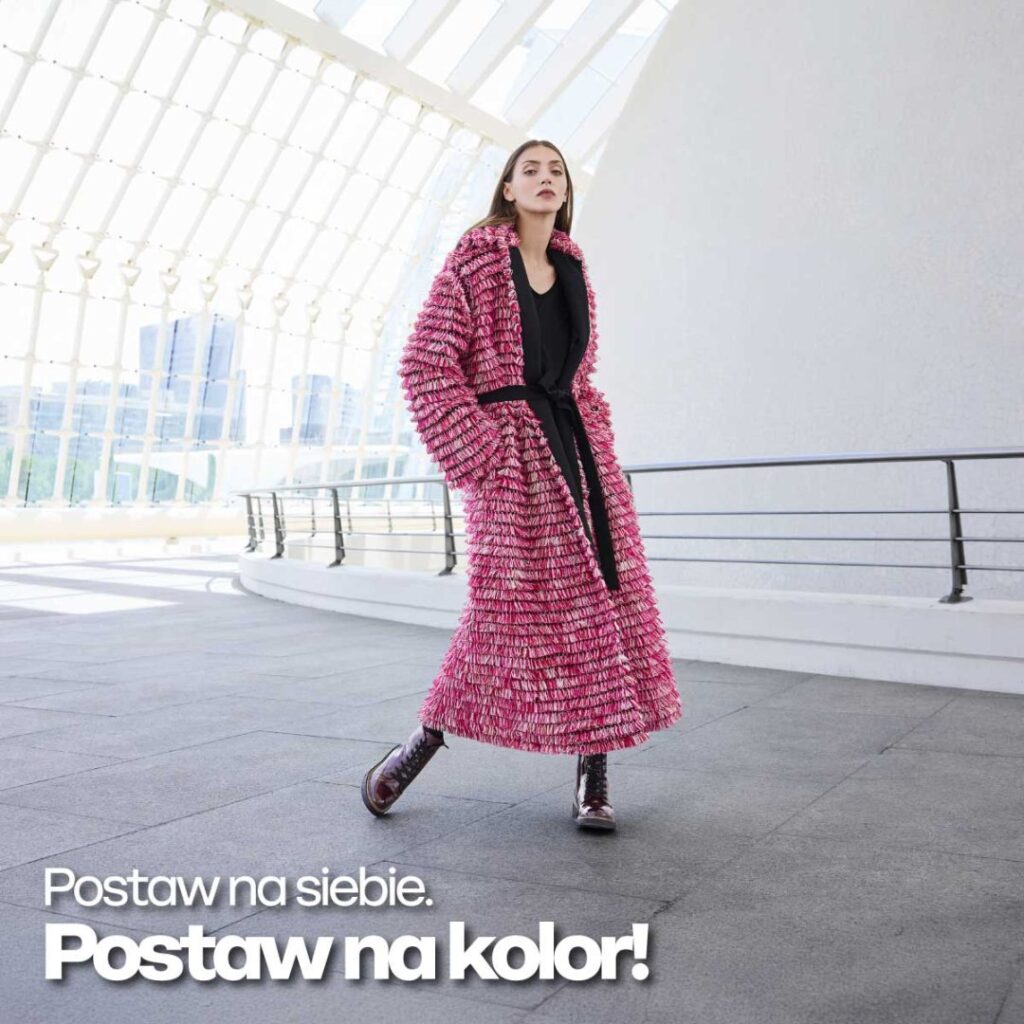 Kobieta w różowym płaszczu idzie w nowoczesnym wnętrzu.