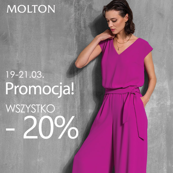 Kobieta w różowym kombinezonie na tle szarej ściany.