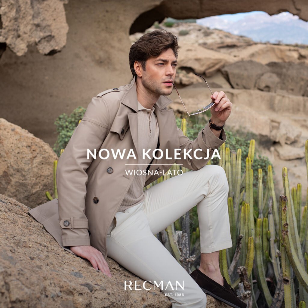 Mężczyzna w beżowym płaszczu siedzi na skałach z okularami przeciwsłonecznymi.