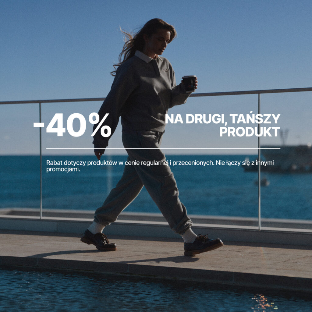 Kobieta spacerująca nad morzem z kubkiem w ręku.