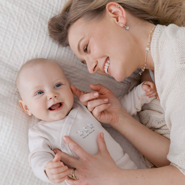 Mama leży obok uśmiechniętego niemowlęcia na łóżku.